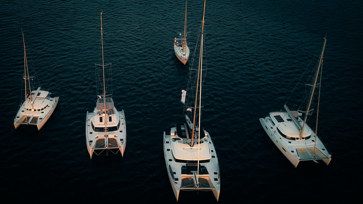 Looking to buy a yacht in charter? Here’s what you need to know about yacht charter ownership Several sleek catamarans docked in a marina, showcasing the benefits of yacht charter ownership, where vessels are rented out when not in use, offering a balance of personal sailing enjoyment and financial gain.